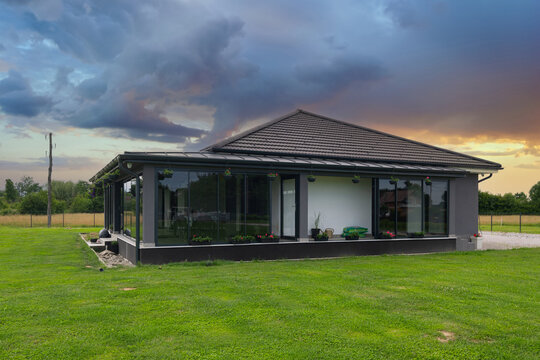 Modern single story house with glass porch and large lawn at sunset in rural setting