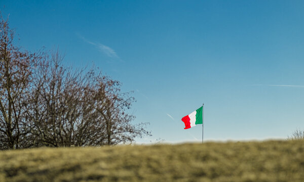 Italian national flag waving above rural landscape under clear sky symbol of identity.