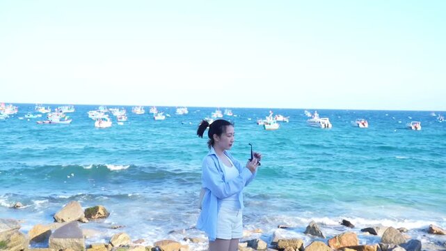 Asian woman enjoying summer vacation at the beach, wearing sun hat and sunglasses, smiling with blue ocean background