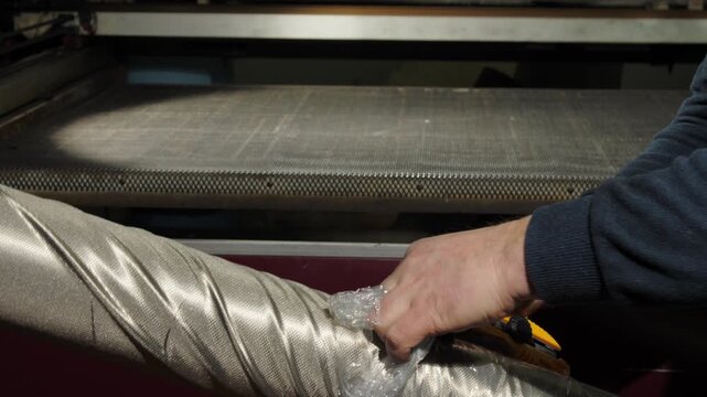 Man pulls plastic foil away from electromagnetic field shielding fabric. Worker prepares EMF radiation-reducing textile for further processing