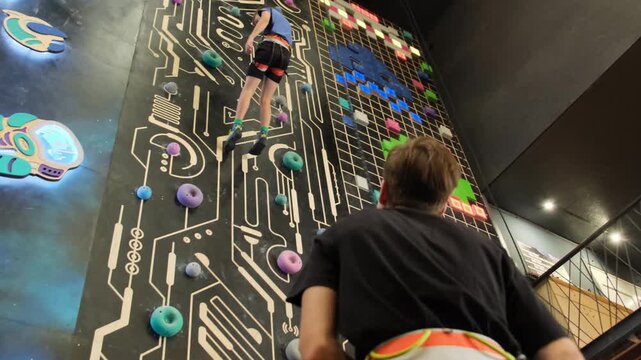 Coach closely monitors safe descent of young athlete from climbing wall. Professional athlete helps beginner get down to ground slow motion