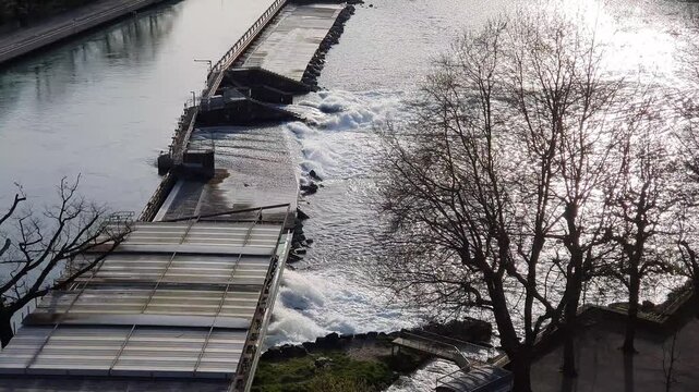 Horizontal footage of water flowing through a small river dam in a European city to generate hydroelectric power and mitigate flooding
