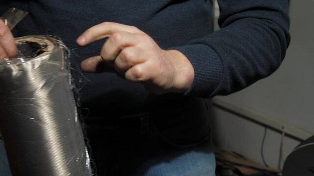 Man unrolls plastic foil from roll of electromagnetic shielding fabric. Worker focus on ensuring integrity of EMF radiation-reducing textile