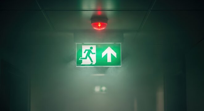 Emergency exit sign glowing in dark corridor indicating safety evacuation and escape route concept