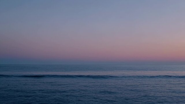 Serene ocean waves gently rolling towards the shore at dusk, with a gradient sky transitioning from soft pink to deep blue over the calm water surface