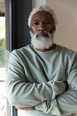 African American Senior man posing with arms crossed, wearing sage sweatshirt beside window at home © wavebreak3