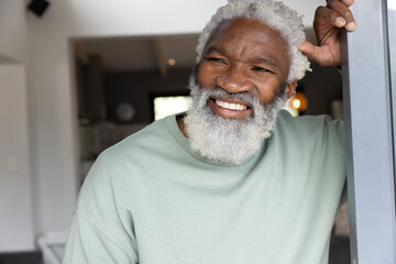 Senior African American man leaning on doorframe at home, wearing light green sweatshirt, smiling © wavebreak3