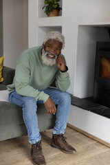 Obraz premium Senior African American man sitting on sofa smiling touching face wearing sage crewneck near stove