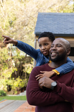 African American father and son standing on deck in yard, father wearing watch, child pointing left