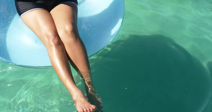 Senior woman shifting weight on blue float, dipping toes into turquoise water, showing anklet