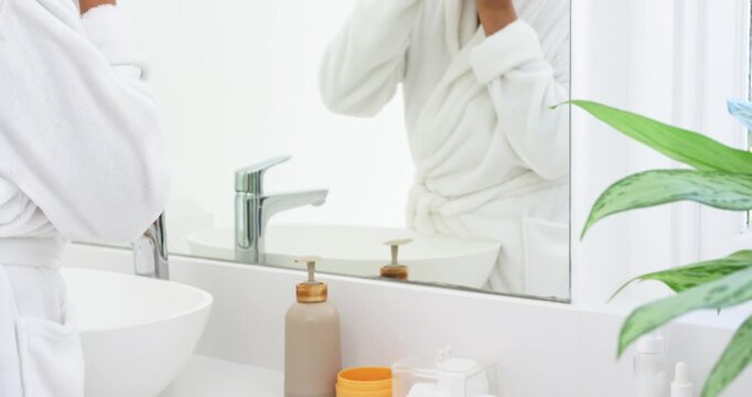 African senior woman in white robe checking mirror and applying red under-eye patches for eye care
