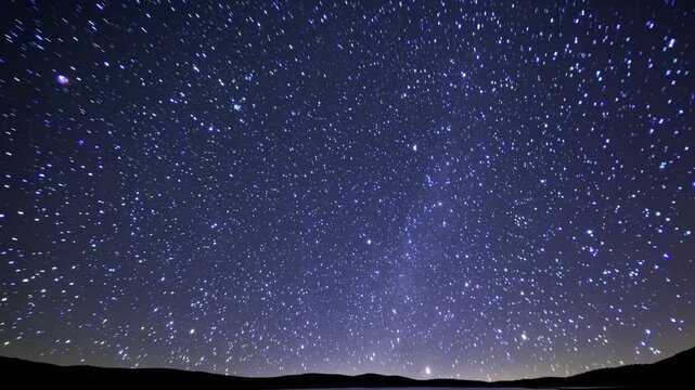 Night sky filled with stars gradually shifting in view over a dark landscape, showcasing the beauty of the cosmos in a serene outdoor setting