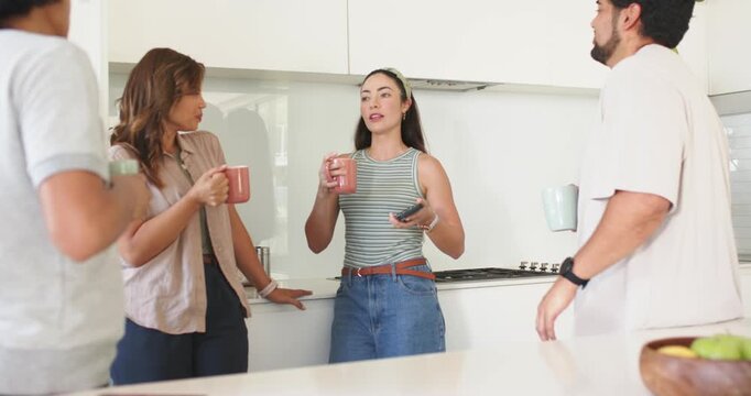 Friends at kitchen island holding mugs, center woman showing smartphone, sharing housemate news