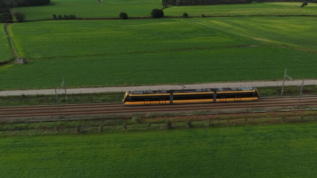 Aerial view of a vibrant yellow train slicing through the lush, green fields creating a stark contrast, Vila do Conde, Portugal.