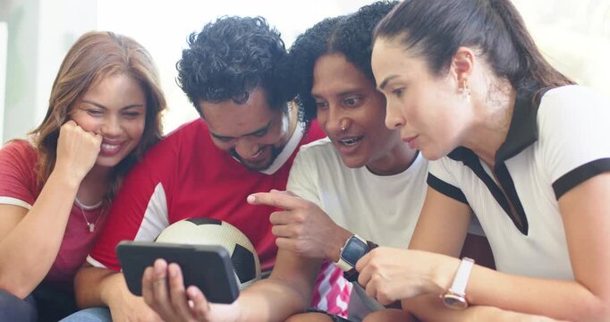 Diverse friends on couch watching phone as man with soccer ball tilting phone sharing match clip