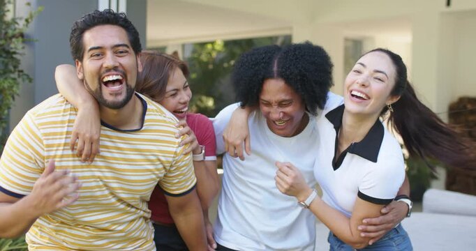 Diverse friends responding to open door at entrance, laughing, linking arms and posing for camera