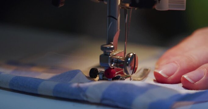 Close-up of hands sewing blue fabric on a machine. The steady rhythm of the needle and careful guidance create a flawless line of stitches, showcasing expert craftsmanship. 60 fps 4k footage.