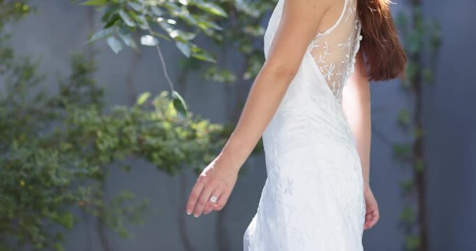 Camera rolling, woman posing in garden in white lace gown, turning, showcasing sheer back, smiling