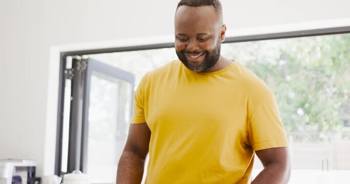 Mid-adult African man in yellow tee smiling then scooping rice into meal containers for meal prep