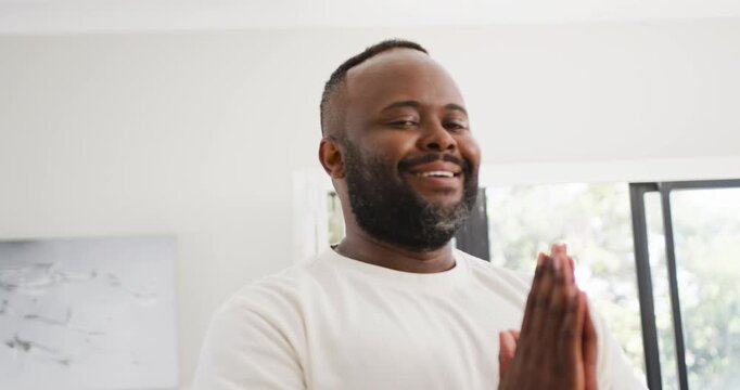 Mid-adult African man in tee holding palms breathing opening eyes smiling ending meditation at home