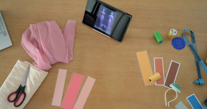 Camera panning across wooden table revealing pink fabric and scissors with laptop sketch for design