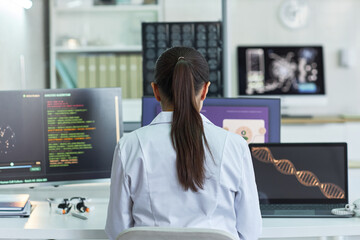 Rear view of young adult woman scientist analyzing medical data, genome visuals, coding screens in...