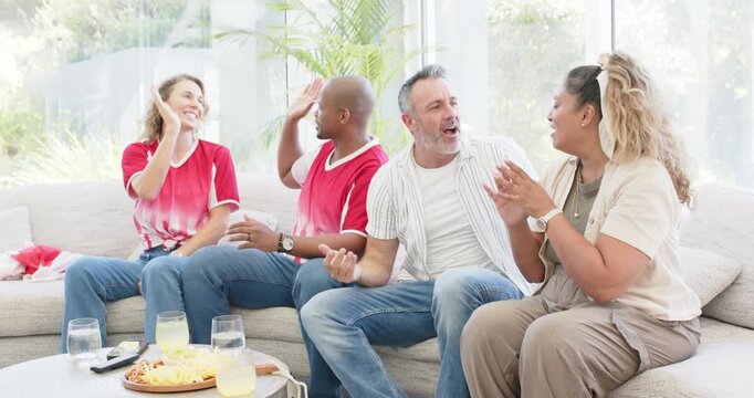 Diverse friends clapping at TV, trading high-fives and fist bumps on sofa near snacks and remote