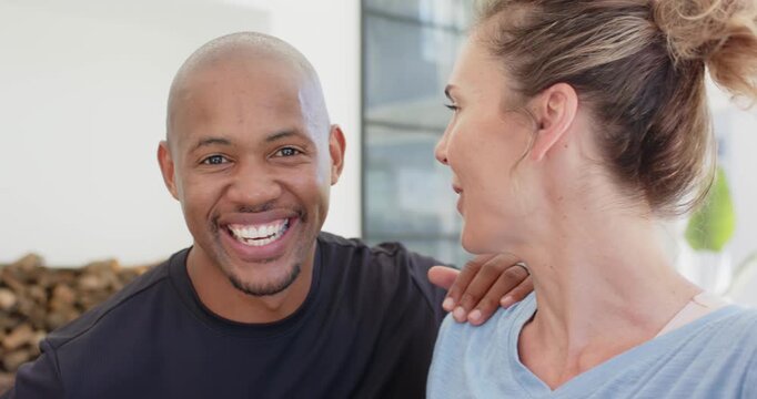 Diverse couple laughing at home while woman raising phone for selfie, man placing hand on shoulder