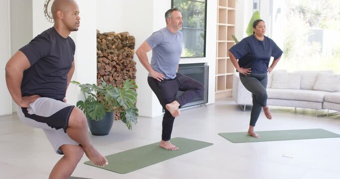 Diverse group keeping one-leg balance on green mats while teacher entering cueing squat for balance