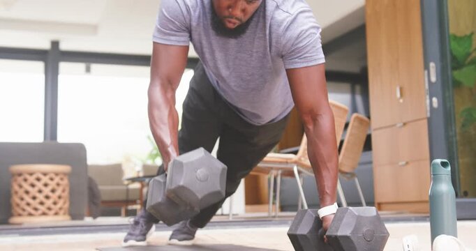 African American man in gray tee holding plank, alternating dumbbell rows on mat for core strength
