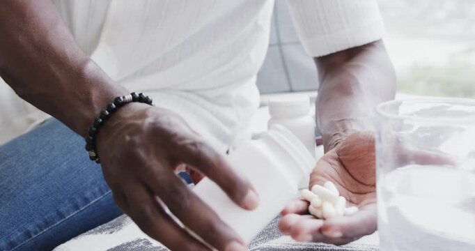 Male pouring pale capsules from white pill bottle at table on patterned cloth wearing shirt