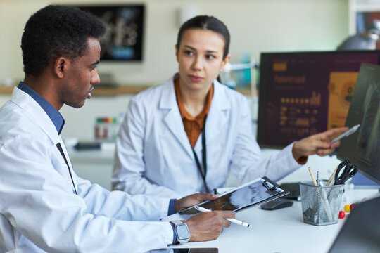 African American male doctor and Asian female doctor reviewing xray scans on monitor, discussing diagnosis and treatment planning. Ideal for healthcare teamwork, radiology, medical consulting