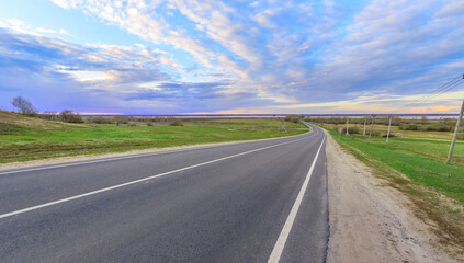 Fototapeta premium Asphalt road curves gently through open fields