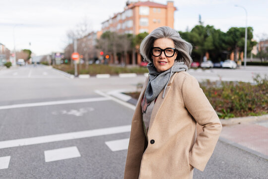 Confident woman with gray hair walking on city street in autumn