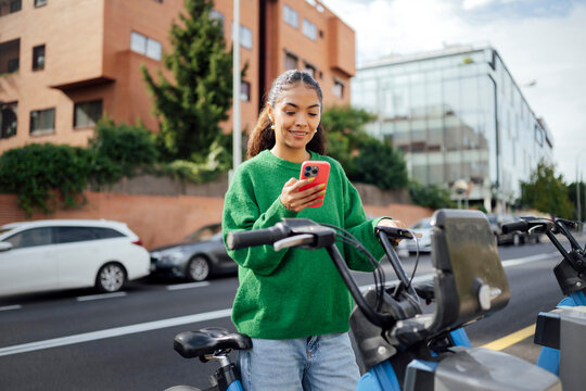 Woman using bike sharing app on smartphone outdoors in city