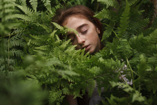 Teenager with freckles resting peacefully among fern plants outdoors