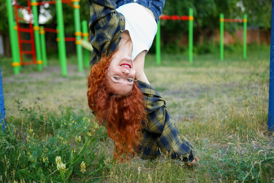 Smiling woman with red curly hair hanging upside down on playground bars