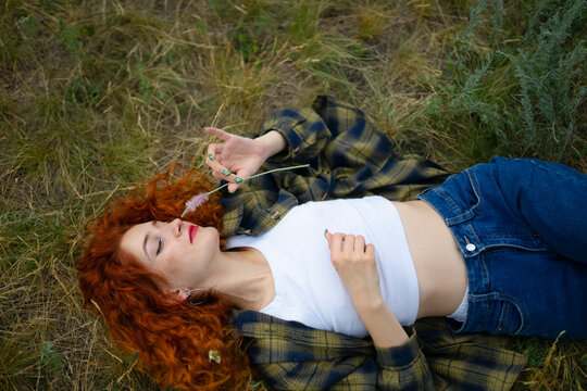 Red haired woman lying in grass with wildflower in summer