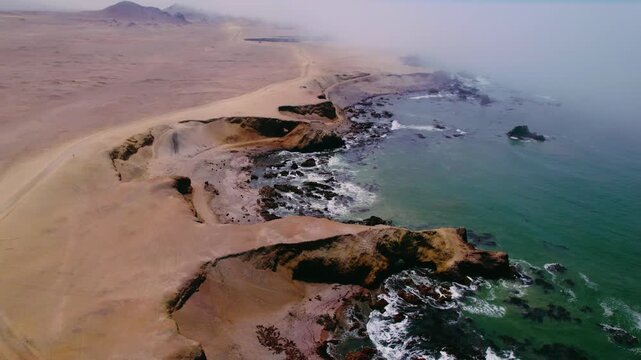 An aerial perspective captures Peru's rugged desert coastline. Waves crash continuously against sandy beaches and rocky outcrops.