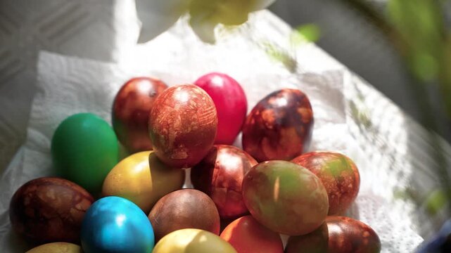 A vibrant collection of multicolored Easter eggs resting on a paper towel, lit by soft sunlight. The close-up shot captures rich textures and shadows, creating a festive mood.