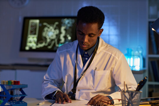 Medium shot of African American male scientist reviewing documents in laboratory, conducting research analysis. Suitable for healthcare marketing, biotech reports, medical innovation campaigns