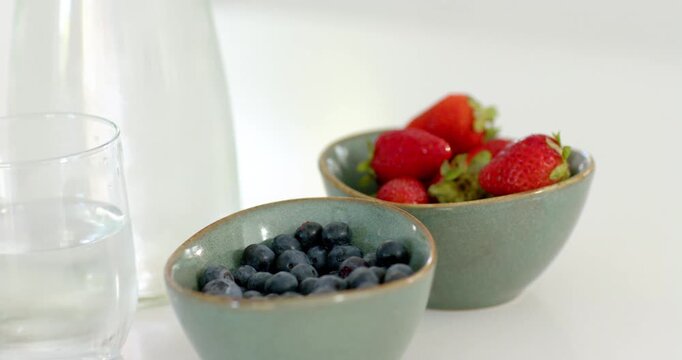 Camera shifting and zooming, moving blueberry and strawberry bowls on countertop to highlight fruit