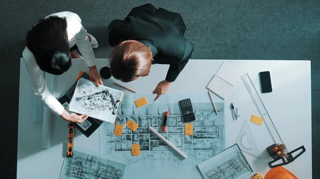 Time lapse of skilled project manager holding project plan and explain house design to architect engineer at meeting table with equipment, ruler, safety helmet and laptop scatter around. Alimentation.