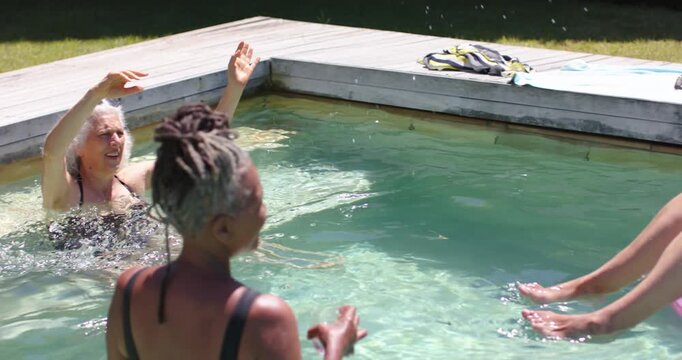 Tossing woman on pink ring hurling beach ball over home pool, friends in swimwear catching, playing