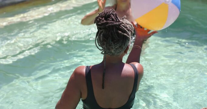 Raising ball, float woman and friends passing beach ball at backyard pool in swimsuits, cooling off