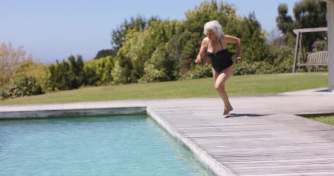 Jumping Senior in black one-piece suit diving into pool after friends cheer, pink float, copy space