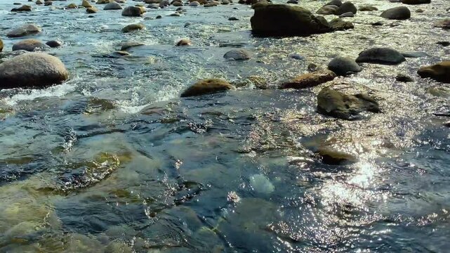 Heavy water stream flows through rocks in riverbed at morning sunlight
