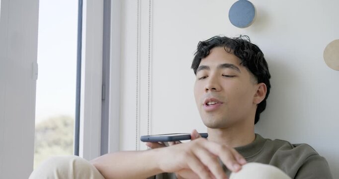Asian man reclining on window seat opening eyes, looking outside, raising phone, tapping messages