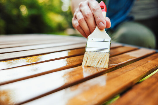 Hand applying oil to wooden sunbed with paintbrush outdoors