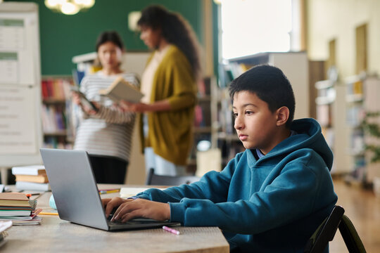 Boy studying on laptop in classroom with two other students in the background